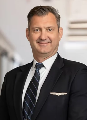 Professional man in dark suit with striped tie and pilot wings pin smiling in corporate headshot