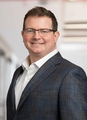Professional man in glasses wearing dark blue blazer and white shirt smiling in modern office setting