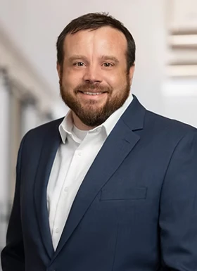 Professional man with beard wearing navy blue blazer and white shirt smiling in office setting