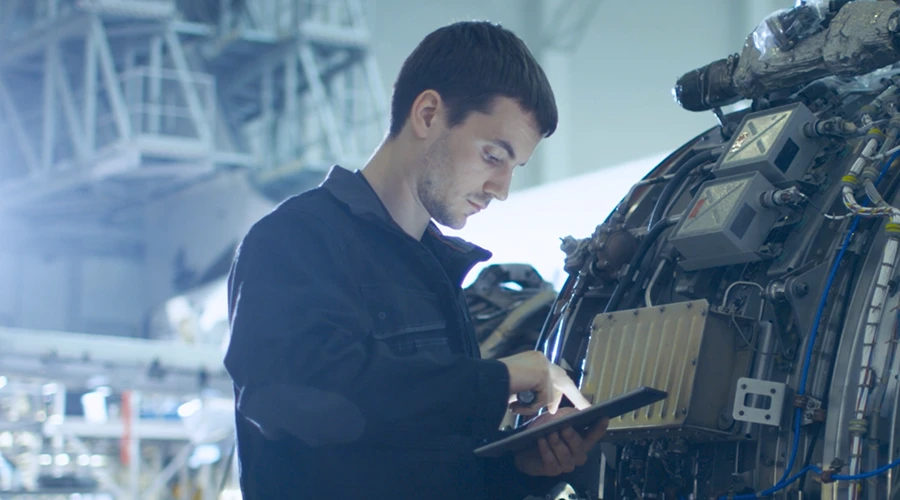 Aircraft mechanic reviewing data on tablet while inspecting jet engine in aviation maintenance hangar