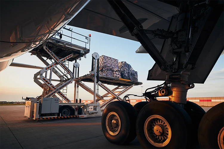 Cargo being loaded into aircraft belly using scissor lift platform at sunset on airport tarmac