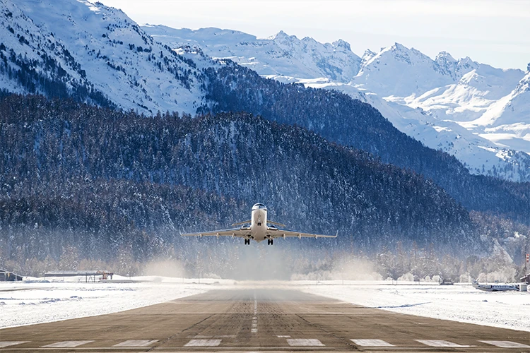 Private jet taking off from snowy mountain runway with dramatic Alpine peaks in background