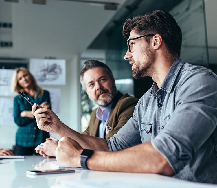 Business professionals in meeting discussing data at conference table with woman standing in background