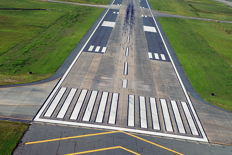 Aerial view of airport runway with white threshold markings and centerline stripes surrounded by green grass